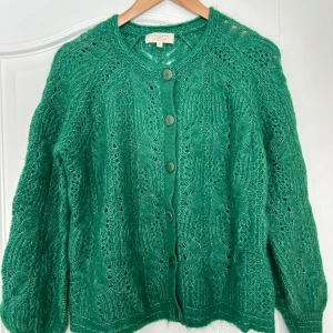 Grön stickad kofta från Sézane - Säljer en superfin grön stickad kofta från Sézane. Den har ett vackert mönster och knappar framtill. Perfekt för höst och vår när du vill vara både stilren och bekväm. Materialet är en blandning av polyamid, ull och elastan vilket gör den både mjuk och hållbar. Passar perfekt till både jeans och kjol!