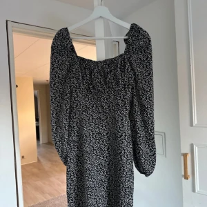 Svart blommig klänning - Säljer en superfin svart klänning med små vita blommor. Den har långa ärmar och en bekväm passform, perfekt för både vardag och fest. Klänningen är i nyskick och passar perfekt till höst och vår. Ett måste i garderoben för dig som älskar blommiga mönster!