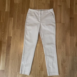  kostymbyxor - Säljer ett par stilrena beige kostymbyxor från H&M i storlek 40. Byxorna har en klassisk rak passform och är perfekta för både kontoret och festligare tillfällen. De är tillverkade i ett bekvämt material och har en diskret ficka bak. Perfekta för vår och sommar!