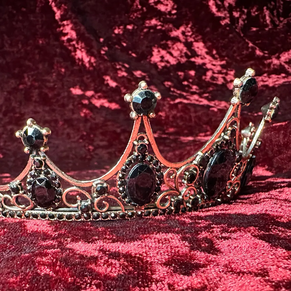 En krona / tiara värdig en vampyrdrottning, mörkeralv eller gothprinsessa. Vacker och välgjord med glittrande svarta stenar & strass mot mörkt guldfärgad ram. Bredd 14,5 cm, båglängd 32 cm, höjd längst fram 5 cm.  Gediget gjord, bekväm att bära. . Accessoarer.