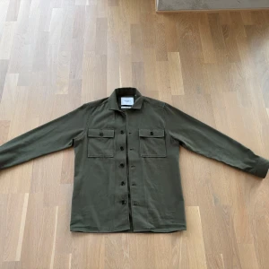Olivgrön overshirt från Les Deux - Säljer en stilren olivgrön overshirt från Les Deux. Perfekt för lager-på-lager-stil ! Nypris 1400 kr. Sparsamt använd (fyra-fem ggr). Fint skick 
