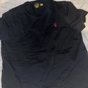 Svart t-shirt från Polo Ralph Lauren - Säljer en svart t-shirt från Polo Ralph Lauren med röd logga på bröstet. T-shirten har en rund hals och är i en custom slim fit modell. Perfekt för en stilren look självklart äkta. Ny pris 1099 mitt pris 750. Köpt i julas