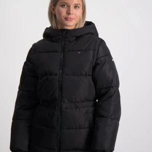 Svart dunjacka med avtagbara ärmar - Snygg svart dunjacka från Tommy Hilfiger med avtagbara ärmar och huva. Jackan har en dragkedja framtill och är perfekt för kyliga dagar. Den är både praktisk och stilren, vilket gör den till ett måste i garderoben.