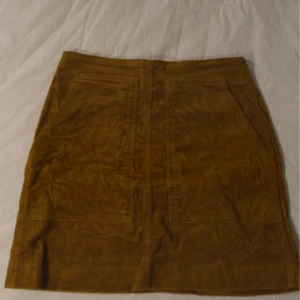 Mustard manchesterkjol från Uniqlo - Snygg mustard manchesterkjol från Uniqlo med dragkedja bak. Kjolen har en klassisk design med en kort längd och är tillverkad i bomull med en liten del elastan för extra komfort. Perfekt för att ge en retro touch till din outfit!