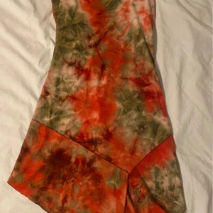 Färgglad klänning från Xanaka - Säljer en färgglad klänning från Xanaka med ett unikt mönster i orange, grönt och beige. Klänningen har en asymmetrisk nederkant och är ärmlös, vilket ger en somrig känsla. Perfekt för dig som vill sticka ut med en bohemisk stil.