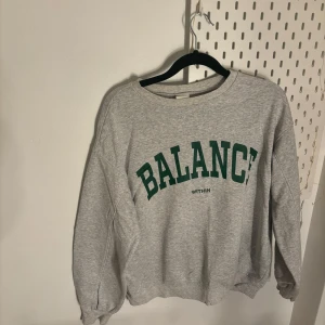 Grå sweatshirt med text - Säljer en grå sweatshirt med grön text 'BALANCE' på framsidan. Tröjan har långa ärmar och en rund halsringning. Perfekt för en avslappnad stil.