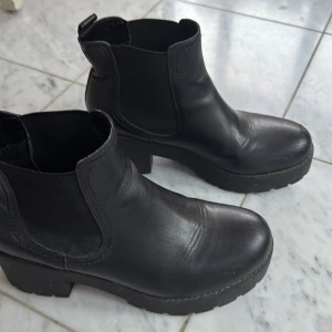 Svarta chelsea boots - Snygga svarta chelsea boots i skinn med grov sula och elastiska paneler på sidorna för enkel på- och avtagning. Lite färg slitage på vänstra sko fransida men annars hela och rena. Använda några gånger. 