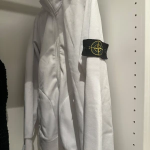 Stone Island kofta - Säljer en stilren vit kofta från Stone Island med dragkedja och fickor framtill.  Den är fantastiskt snygg och passa bra med jeans. Den sitter bra vid midjan och ärmarna. Den är i mycket bra skicka då den är ganska ny och har inte använt den så mycket.