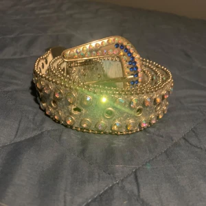 Rhinestone bälte  - Snyggt glittrigt bälte dekorerat med strass och nitar. Bältet har en iögonfallande spänne med blå och klara stenar. Perfekt för att ge en extra touch till din outfit.