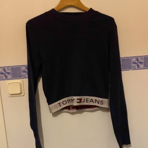 Svart ribbad tröja från Tommy Jeans - Snygg svart ribbad tröja från Tommy Jeans med elastisk kant och logga i nederkant. Perfekt för en stilren look.