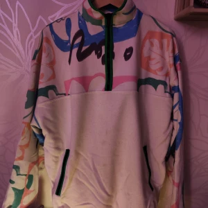 Färgglad tröja med dragkedja från ASOS DESIGN - Säljer en unik och färgglad tröja från ASOS DESIGN med dragkedja och abstrakt mönster i rosa, blått, grönt och svart. Perfekt för att liva upp garderoben!