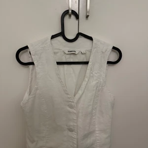 Vit väst från KappAhl - Snygg vit väst från KappAhl med knappar framtill. Perfekt för att lägga till en stilren touch till din outfit. Västen har en v-ringad design och är tillverkad i ett lätt material.