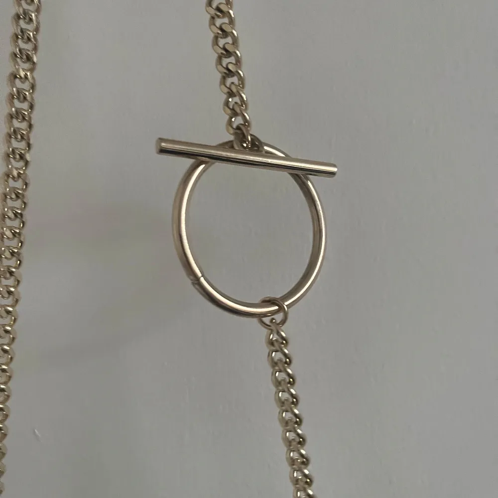 Snygg svart axelväska från Zara med guldfärgad kedja och stilren design. Väskan har en unik stängning med en cirkel och stångdetalj. Perfekt för att ge en elegant touch till din outfit.. Laukut & Käsilaukut.