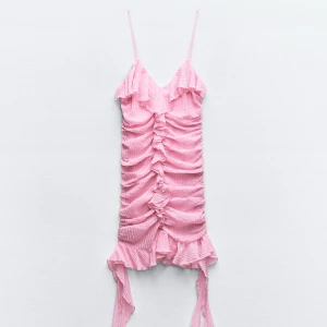 Rosa omlottklänning med volangdetaljer - Söt rosa klänning med smala axelband och volangdetaljer. Klänningen har en omlott-design och är kort, perfekt för sommarens varma dagar. Den har en rynkad effekt som ger en fin textur och stil.