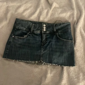 Jeanskjol från Bershka - Säljer en cool jeanskjol från Bershka i mörkblå denim. Kjolen har en rå kant och tre knappar framtill. 