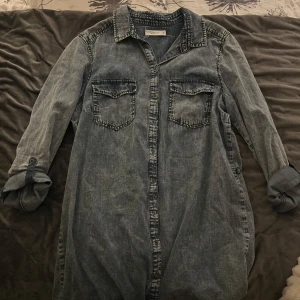 Jeansskjorta från Denim by Linbex - Snygg jeansskjorta/klänning från Denim by Linbex i storlek L. Skjortan har långa ärmar och två bröstfickor med knappar. Perfekt för en avslappnad stil med en klassisk denimlook.Passar mig som vanligtvis bär S