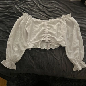 Vit blus från H&M - Säljer en söt vit blus från H&M med långa puffiga ärmar och knytning framtill. Perfekt för en romantisk look eller en somrig dag. Blusen har en croppad passform och elastiska detaljer vid ärmsluten.