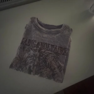 Grå t-shirt från Zadig & Voltaire - Snygg grå t-shirt från Zadig & Voltaire med ett coolt tryck av blommor och en gitarr. Perfekt för en avslappnad stil.
