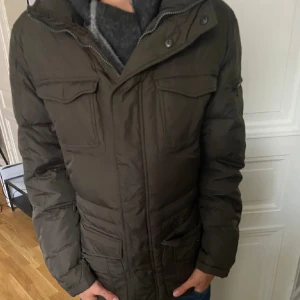 Mörkgrön pufferjacka från Geox - Säljer en mörkgrön pufferjacka från Geox med dragkedja och knappar. Jackan har långa ärmar och flera praktiska fickor framtill. Perfekt för kyligare dagar. Nypris 2200 mitt pris 899