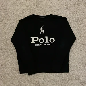 Svart långärmad tröja från Polo Ralph Lauren - Säljer en stilren svart långärmad tröja från Polo Ralph Lauren med det ikoniska logotyptrycket i vitt på framsidan. Perfekt för en avslappnad och trendig look.