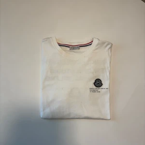 Vit t-shirt från Moncler - Snygg vit t-shirt från Moncler med tryck på både fram- och baksidan. Den har en rund halsringning och är kortärmad. Perfekt för en stilren och modern look.