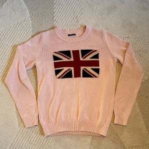 Rosa stickad tröja med flagga - Säljer en rosa stickad tröja med ett stort flagg motiv på framsidan. Tröjan påminner om raulph lauren