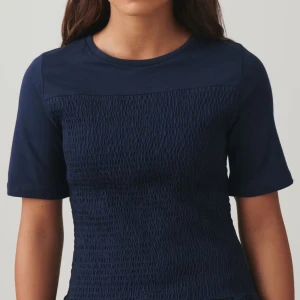 Mörkblå topp med textur - Snygg mörkblå topp med unik textur på framsidan. Toppen har korta ärmar och en rund halsringning, perfekt för en stilren look.