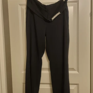 Svarta kostymbyxor - Snygga svarta kostymbyxor med hög midja och rak passform. Perfekta för en stilren look. Byxorna har en dragkedja och knapp framtill.