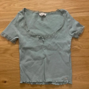 Ljusblå topp med spetsdetaljer - Söt ljusblå topp från Brandy Melville med spetskant vid halsringning och ärmslut. Toppen har korta ärmar och en liten rosett framtill. Perfekt för en avslappnad stil.