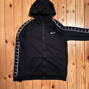 Svart zipkofta från Nike - Säljer en svart hoodie från Nike med dragkedja och huva i storlek 158/170 eller XXS - XS. Den har vita Nike-loggor längs ärmarna och en på bröstet. Enbart använd några fåtal gånger, i princip nyskick.