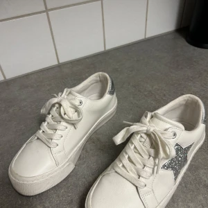 Vita sneakers med glittrig stjärndetalj - Snygga vita sneakers från Next med en glittrig stjärna på sidan och silverdetalj vid hälen. Skorna har snörning och använda endast 1 gång på en avslutning. Köp gärna😊