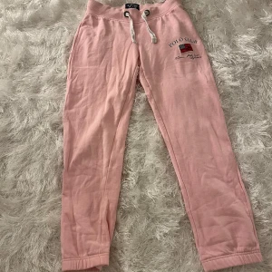 Rosa mjukisbyxor från Vinson Polo Club - Snygga rosa lågmidjade mjukisbyxor från Vinson Polo Club med broderad logga och snörning i midjan. Perfekta för en avslappnad stil. Säljer pga att dom är för korta för mig och jag är 170cm☺️❤️