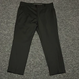 Svarta kostymbyxor - Eleganta svarta kostymbyxor med en klassisk passform. Byxorna har en midwaist-design och är perfekta för formella tillfällen. De har knappar bak och en stilren look.