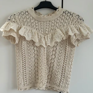 Populär topp från Zara - Charmig beige stickad topp från Zara med vackra spetsdetaljer och volang runt halsen. Den har korta ärmar och ett intrikat mönster som ger en romantisk känsla. Slutsåld överallt och jättefint skick 