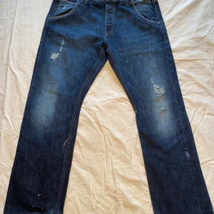 Blå jeans från Jack & Jones - Säljer ett par blå jeans från Jack & Jones, modell Travis Kay Selvage RDD. De har en straight passform med slitna detaljer och en klassisk femficksdesign. Tillverkade i Italien med en snygg tvättad look.