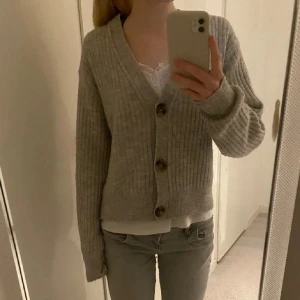 Grå ribbad kofta - Säljer en mysig grå ribbad kofta med knappar framtill. Koftan har långa ärmar och en v-ringad design, perfekt för kyligare dagar. Passar bra till både jeans och kjol.