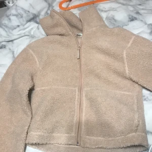 Beige teddyjacka med dragkedja - Mysig beige teddyjacka från H&M med dragkedja framtill. Jackan har en hög krage och långa ärmar, perfekt för kyliga dagar. Den är i storlek XS och ger en avslappnad look.