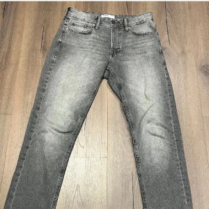 Jack&jones jeans gråa - Snygga grå jeansbyxor med en klassisk straight passform. De har en diskret tvättad look och är utrustade med både dragkedja och knappar. Perfekta för en avslappnad stil. Som nya! Storlek: 30:32