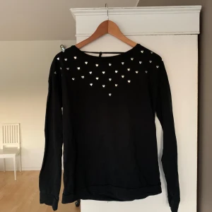Svart tröja med hjärtan - Säljer en svart långärmad tröja dekorerad med små silverhjärtan på framsidan. Tröjan har en rund halsringning och en knytning i ryggen. Priset går att diskutera vid snabb affär. Tveka inte med att höra av dig om du har frågor eller några funderingar. 