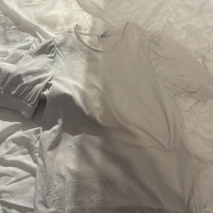 Vit kortärmad topp - Säljer en enkel och stilren vit topp med korta ärmar. Perfekt för en avslappnad look. Toppen har en rund halsringning och är gjord i ett mjukt material.