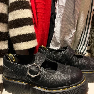 Svarta Dr. Martens skor med spänne - Säljer ett par svarta Dr. Martens skor i skinn med ett unikt spänne på ovansidan. Skorna har den klassiska gula sömmen och en robust sula. Perfekta för en edgy look! Satte i skydd bak för att inte få skavsår, går att ta bort!