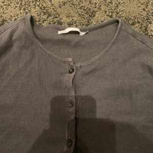 Svart ribbad kofta - Säljer en stilren svart ribbad kofta med knappar framtill. Koftan har långa ärmar och en rund halsringning, perfekt för lager-på-lager-stil. Passar bra till både jeans och kjol.