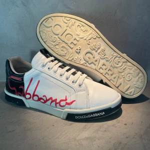 Dolce Gabbana skor - Dolce & Gabbana sneakers i vitt, svart och rött. Snygga och stilrena. Perfekt för vardagligt bruk eller för att klä upp sig lite extra.                                                                            Skick 9/10 små sprickor i läder finns.     nyligen inlämnade hos sneakerstvätten.se(kvitto finns).                               Storlek 40.                                                                               Hör av er vid minsta fundering🙌