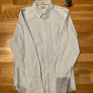 Randig skjorta från Nimbus - Säljer en stilren randig skjorta från Nimbus i blått och vitt. Skjortan är långärmad och har en klassisk krage med knappar framtill. Tillverkad i 100% kammad bomull för en bekväm känsla. Perfekt för en avslappnad men ändå uppklädd look.