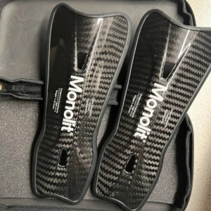 Monolit Benskydd i Kolfiber, 19 cm!! - Säljer ett par Monolit benskydd. Så så så lätta & sköna!! Helt nya! De är i den större längden, 19 cm. Benskydden är tillverkade av kolfiber, vilket gör att de skyddar extra bra jämfört med andra benskydd! De har två ”ventilhål” så att benet kan andas och få bort fukt & värme! Benskydden väger cirka 40 gram, vilket också gör de till världens lättaste benskydd! Fodral och användartips-kort ingår! Nypriset är 789 kr.   Skriv vid frågor/fler bilder!