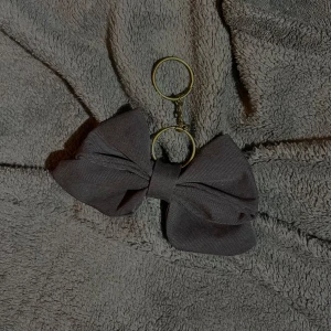 Nyckelring/bagcharm med grå rosett - Snygg nyckelring med en stor grå rosett. Perfekt accessoar för att ge dina nycklar en stilfull touch. Rosetten är gjord av ett mjukt material och fäst vid en guldfärgad/silverfärgad nyckelring. (Vi erbjuder även att mötas upp i söder, huddinge, tyresö, lidingö.)