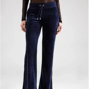 Svarta velourbyxor från Juicy Couture - Snygga svarta velourbyxor från Juicy Couture med glittrande textdetalj på baksidan. Byxorna har en hög midja och dragsko i midjan för justerbar passform. Perfekta för en avslappnad och trendig look.Svarta juicy couture byxor med text, nyskick. Mörkblåa juicy couture byxor, använda men inga synliga defekter. De svarta är i storlek M och de mörkblåa i storlek L. Pga att jag inte använder dom säljer jag båda för 1000kr de svarta- 850kr de blåa-500kr skriv för mer info eller privata bilder.