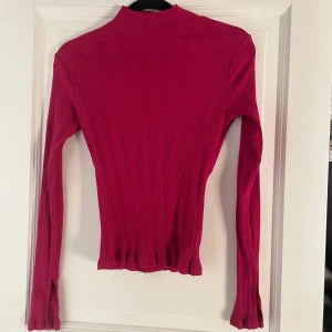 Gina Tricot Rosa tröja storlek S - Rosa ribbad tröja med halvpolo och långa ärmar. Den är gjord av 95% bomull och 5% elastan, vilket gör den både bekväm och stretchig. Perfekt för höst och vår! Tröjan har en stilren design och är i bra skick.
