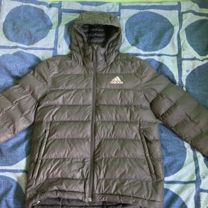 Svart vinterjacka från Adidas - Säljer en snygg och varm svart/grå vinterjacka  från Adidas. Jackan har en dragkedja framtill och en huva för extra skydd mot kyla. Perfekt för kalla höst- och vinterdagar. Den är i väldigt  bra skick och Adidas loggan är reflex! 
