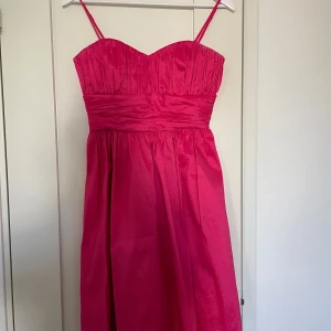 Rosa klänning med smala axelband - Fin rosa klänning från Calvin Klein med smala axelband. Den har en söt hjärtformad urringning och är gjord i ett glansigt material som ger en lyxig känsla. Klänningen har en dragkedja i ryggen för enkel knäppning.